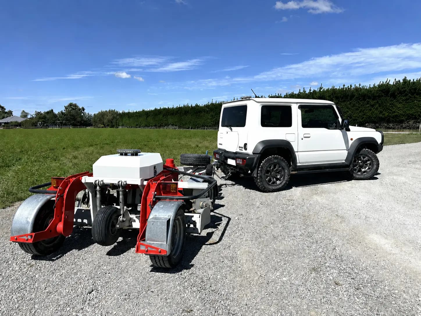 The tow-behind road machine hitched to a small four-wheel drive on a gravel yard